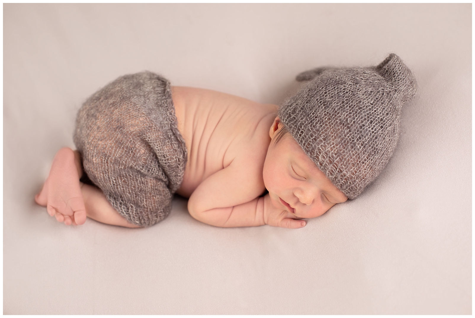 newborn in tushy up pose wearing hat and shorts