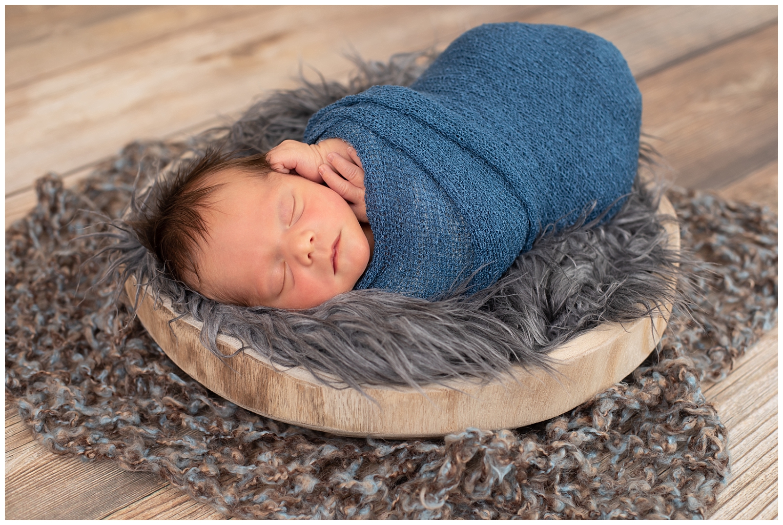 newborn sleeping in wrap on fur in a wooden bowl