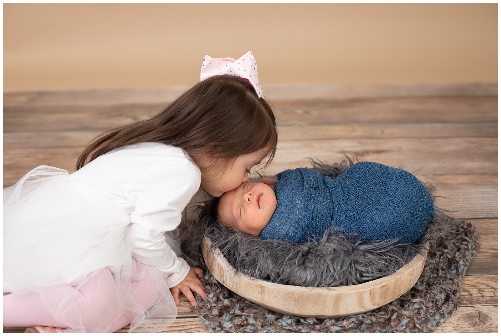 sister in pink dress kissing newborn boy on the forehead