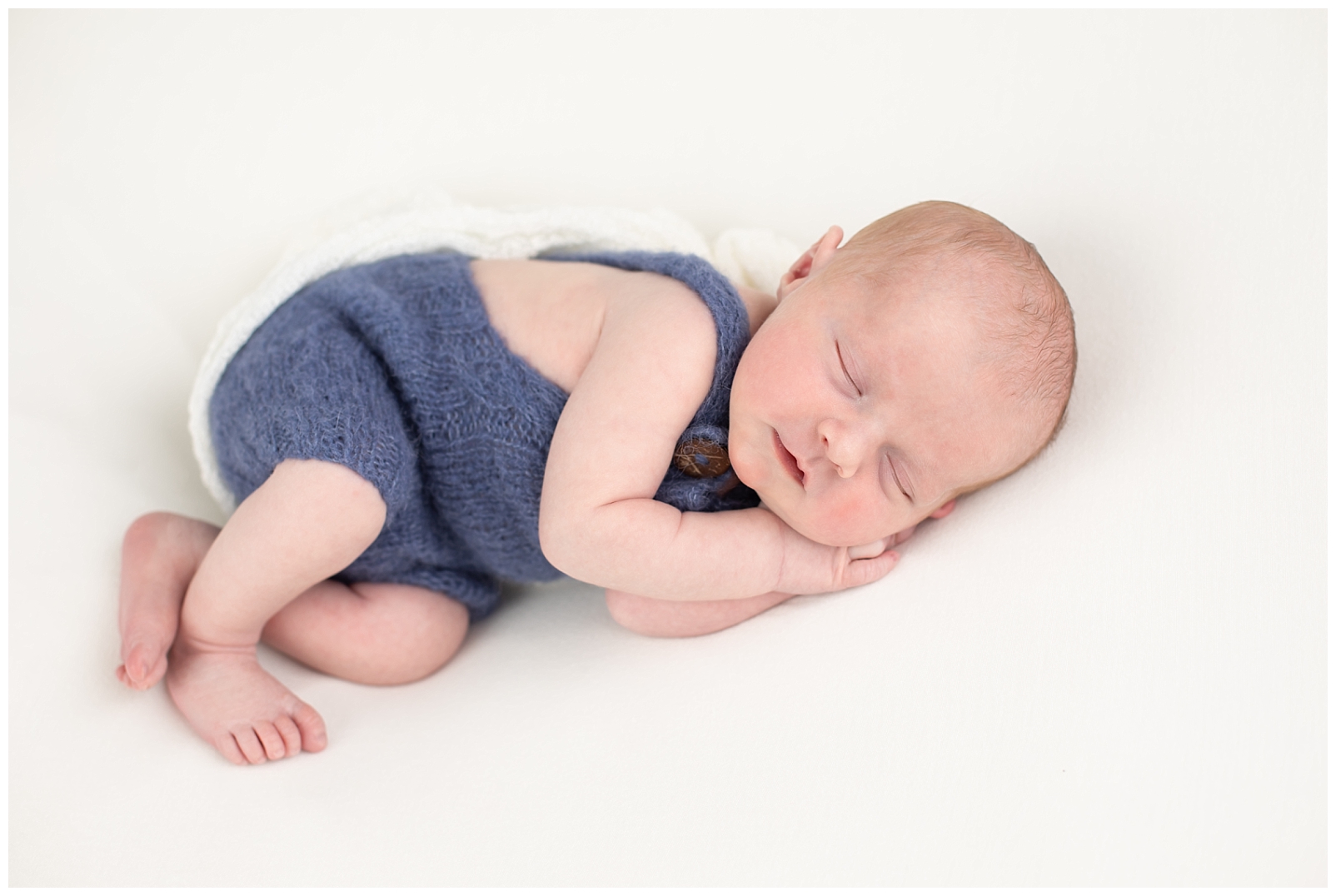 newborn boy with blue overalls and a smile