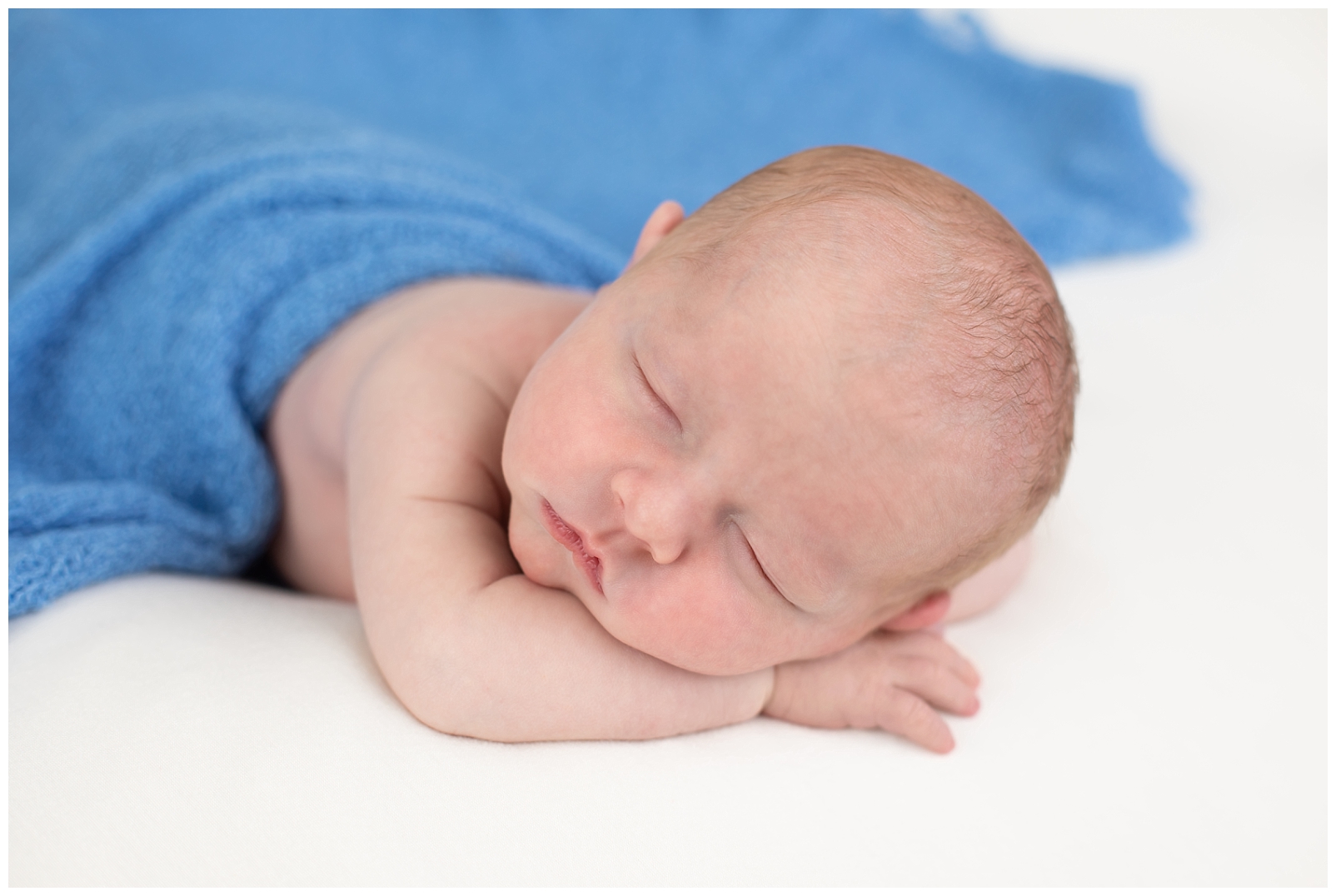 newborn boy chin on hands pose with light blue wrap