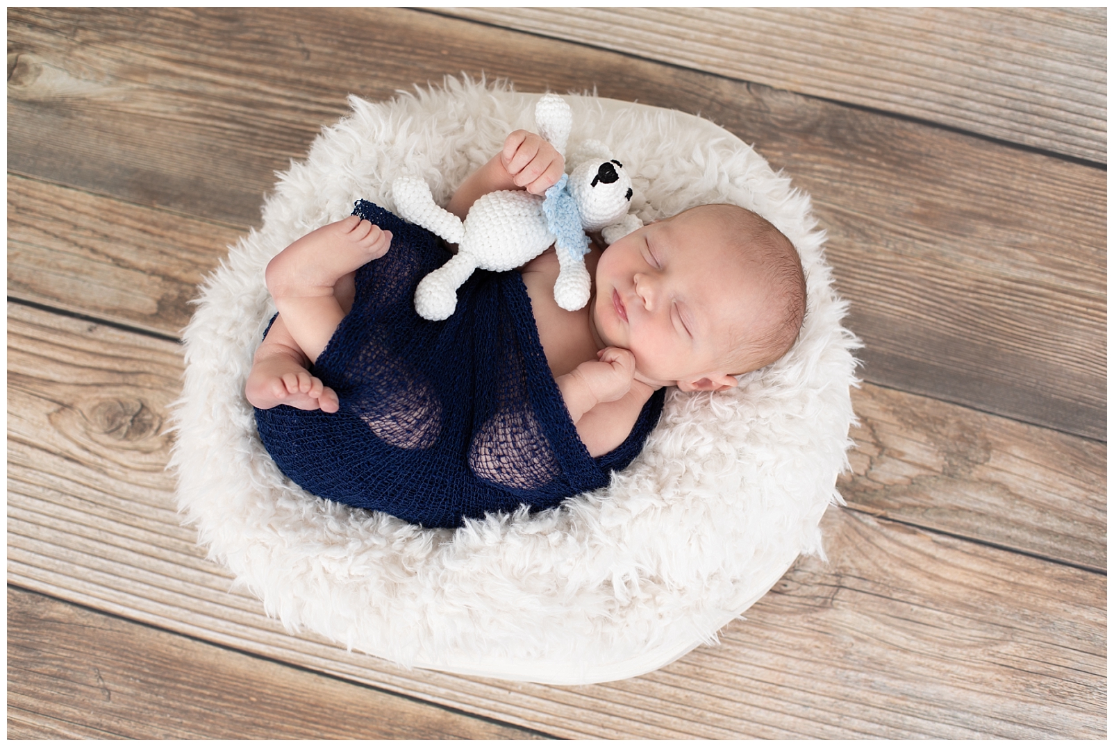 Newborn boy in blue wrap holding a teddy bear