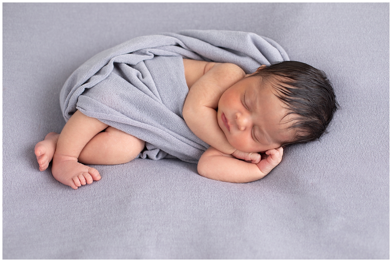 newborn girl sleeping on her side with a gray wrap