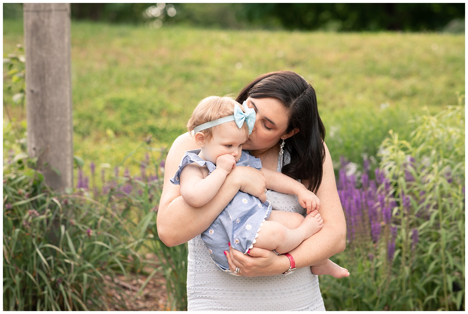 Mom holding daughter near a stone wall with purple flowers