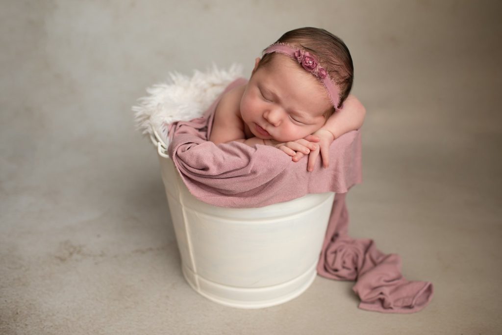 Newborn with chin on hands in bucket with a mauve floral headband