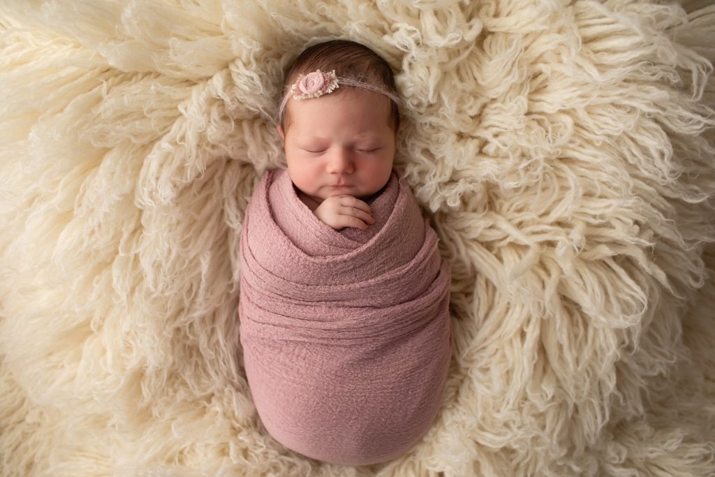 newborn wrapped in mauve on a flokati rug