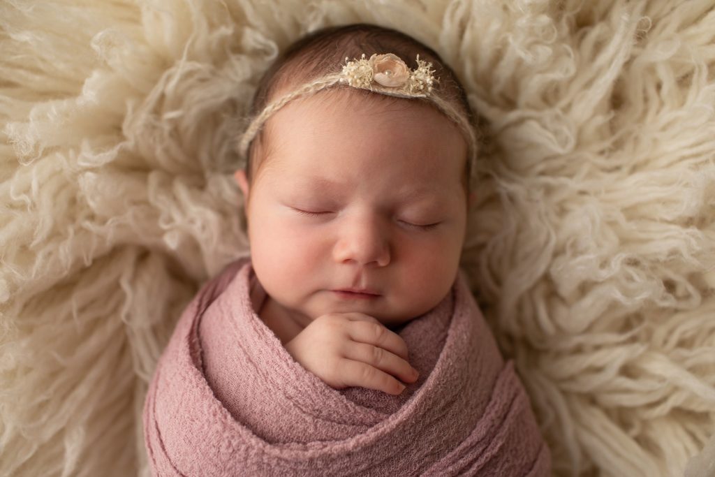 newborn wrapped in mauve on a flokati rug wearing Emiliana headband