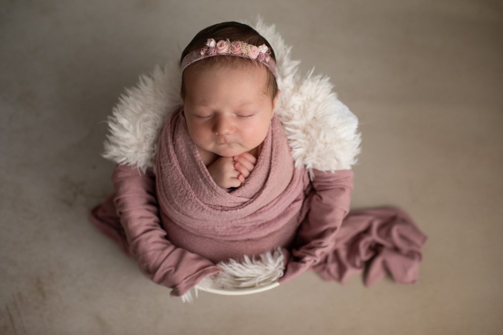 Newborn wearing Hattie headband posed in a fur lined bucket