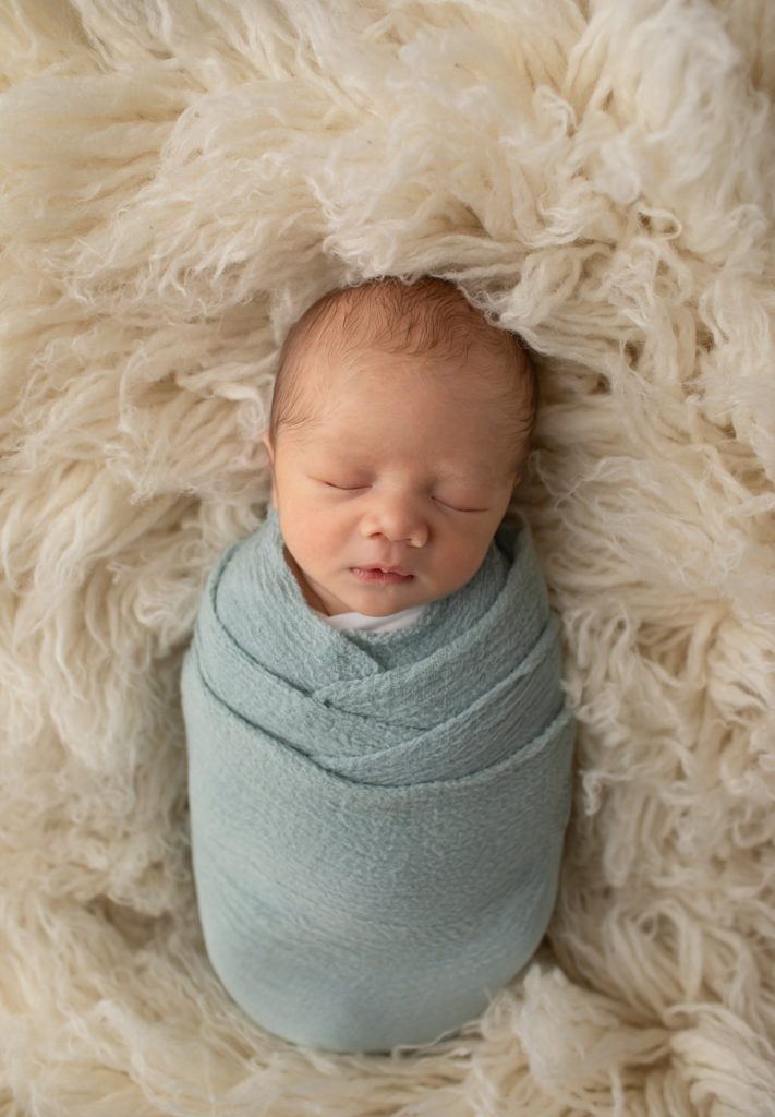 newborn boy wrapped in blue on a flokati