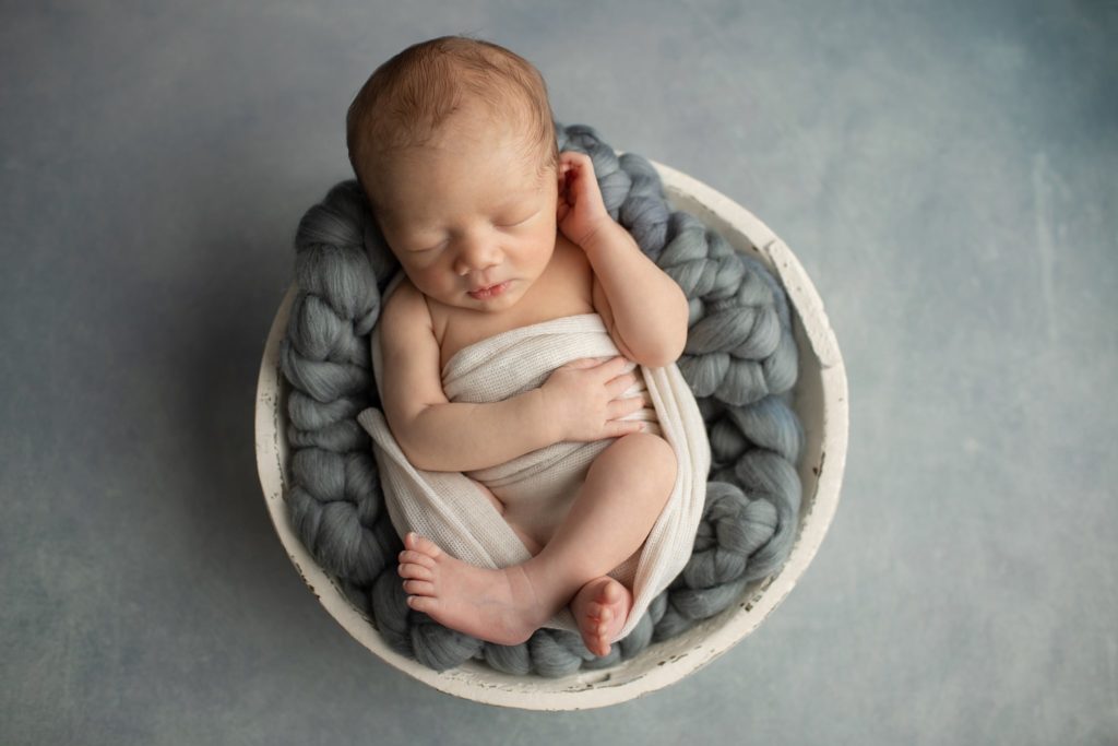 Newborn boy in a bowl with chunky gray wool knit blanket