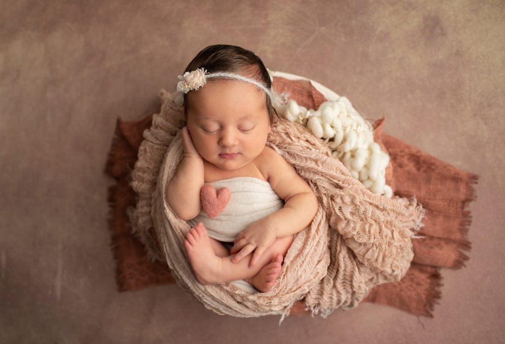 Newborn with a felted heart in a bowl of fabric