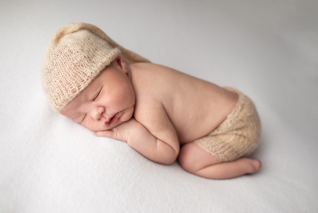 newborn wearing hat and sleeping on white fabric