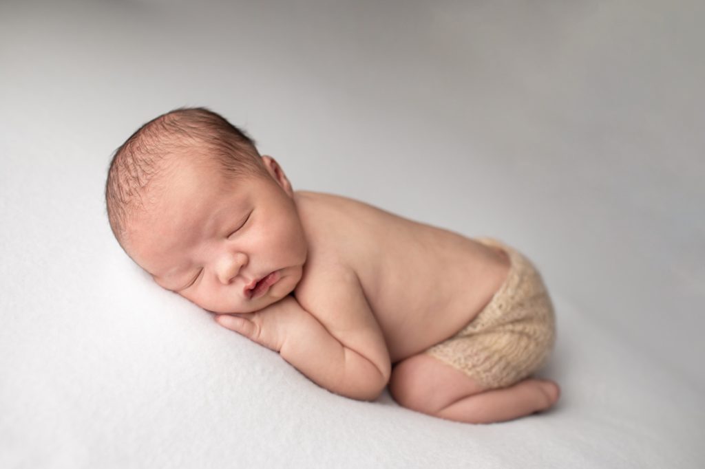 newborn sleeping on white fabric