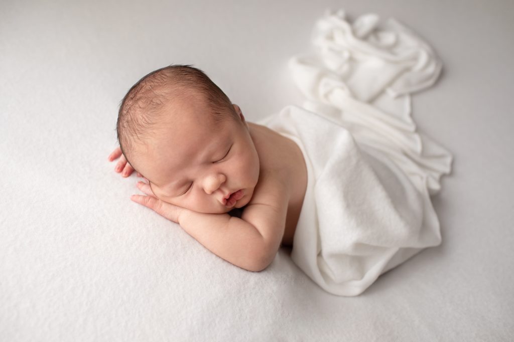 newborn sleeping on white fabric