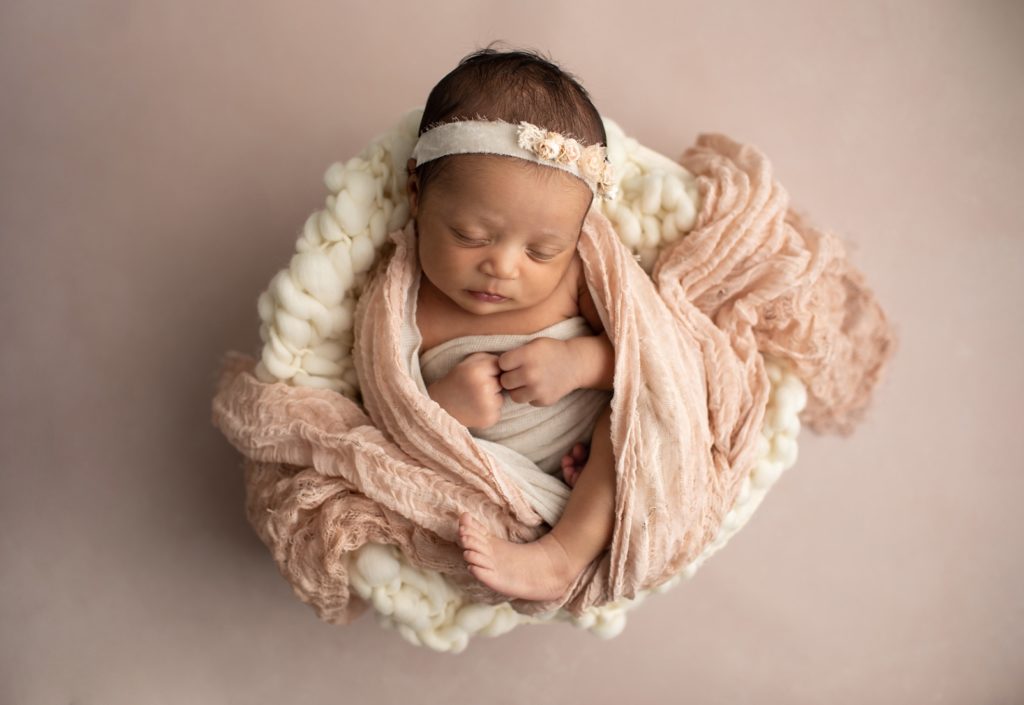 newborn swaddled in blush and in a bowl