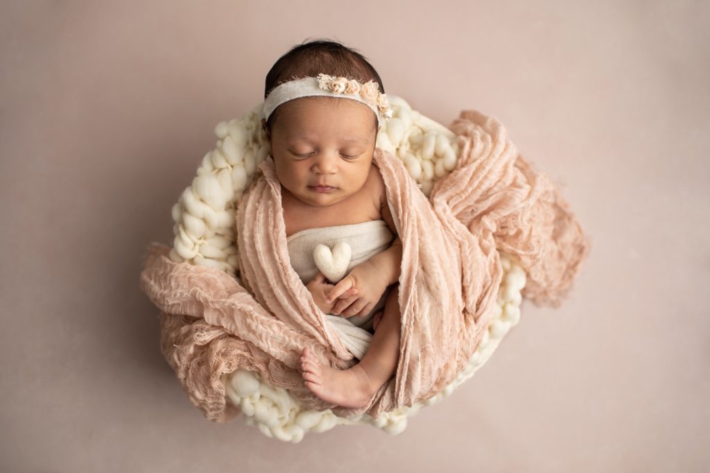 newborn swaddled in blush and in a bowl with a felted heart in hand
