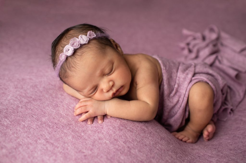 newborn lying on belly on hands on a purple blanket