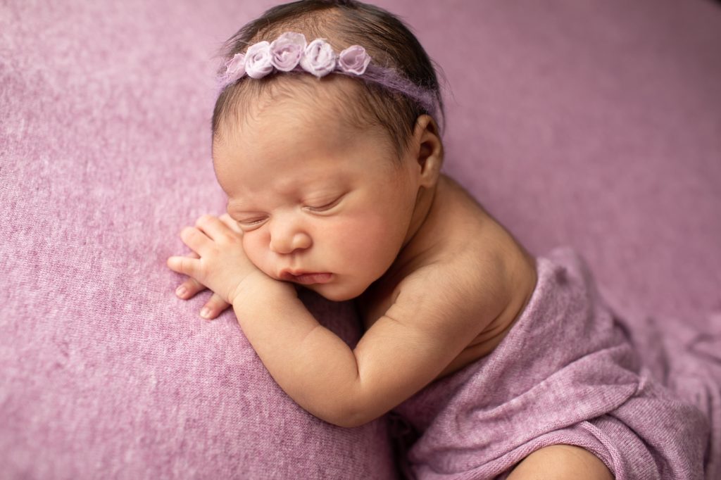 newborn lying on belly on hands on a purple blanket