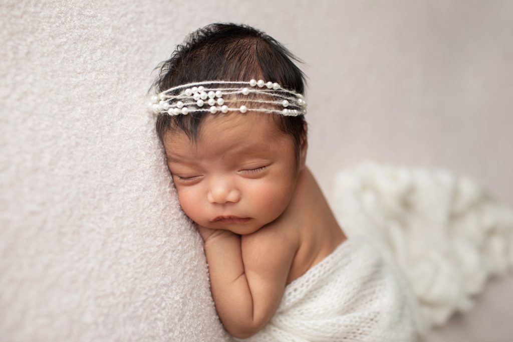 newborn wrapped in white with pearl headband