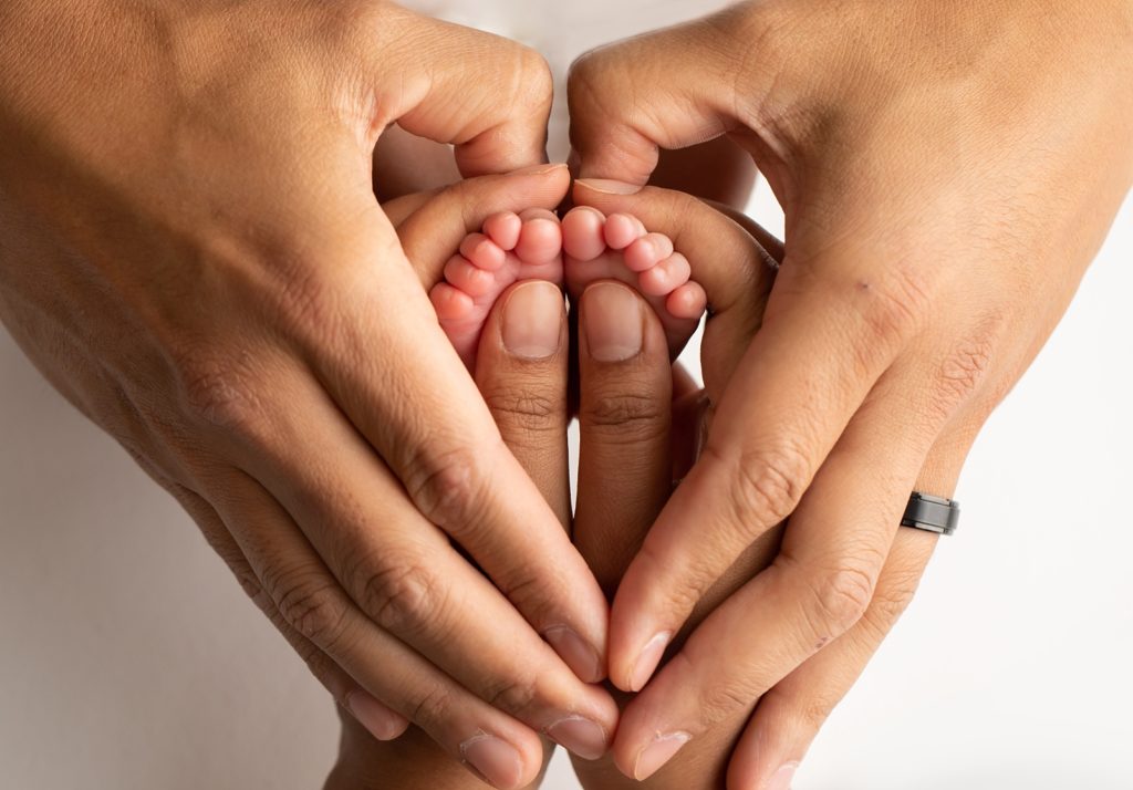 mom's and dad's hands holding newborn feet in the shape of a heart