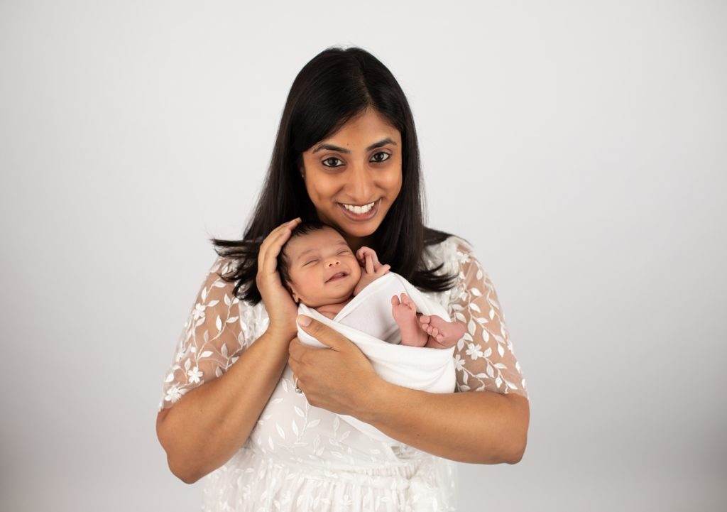 mom holding newborn baby in wrap with baby smiling