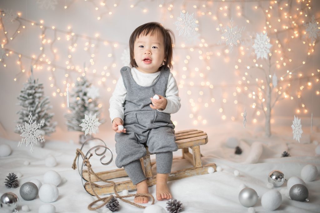 baby in gray overalls on small sled in snow