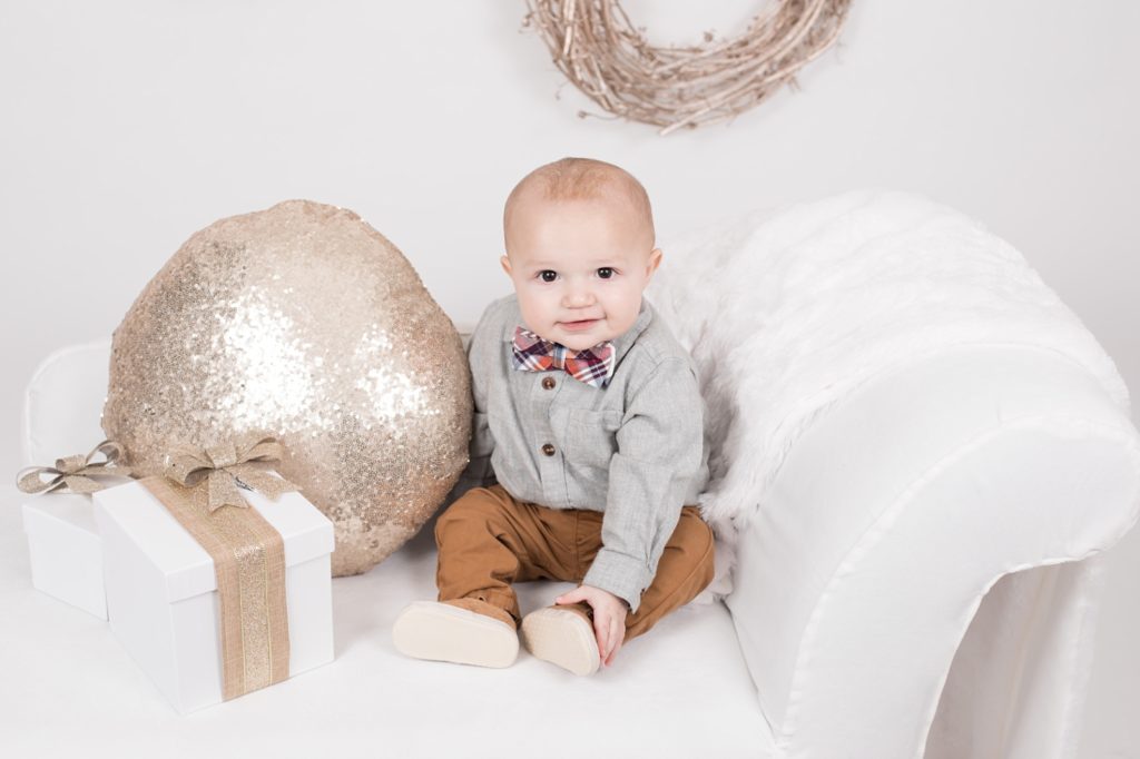 baby boy sitting on white chair with gold pillow
