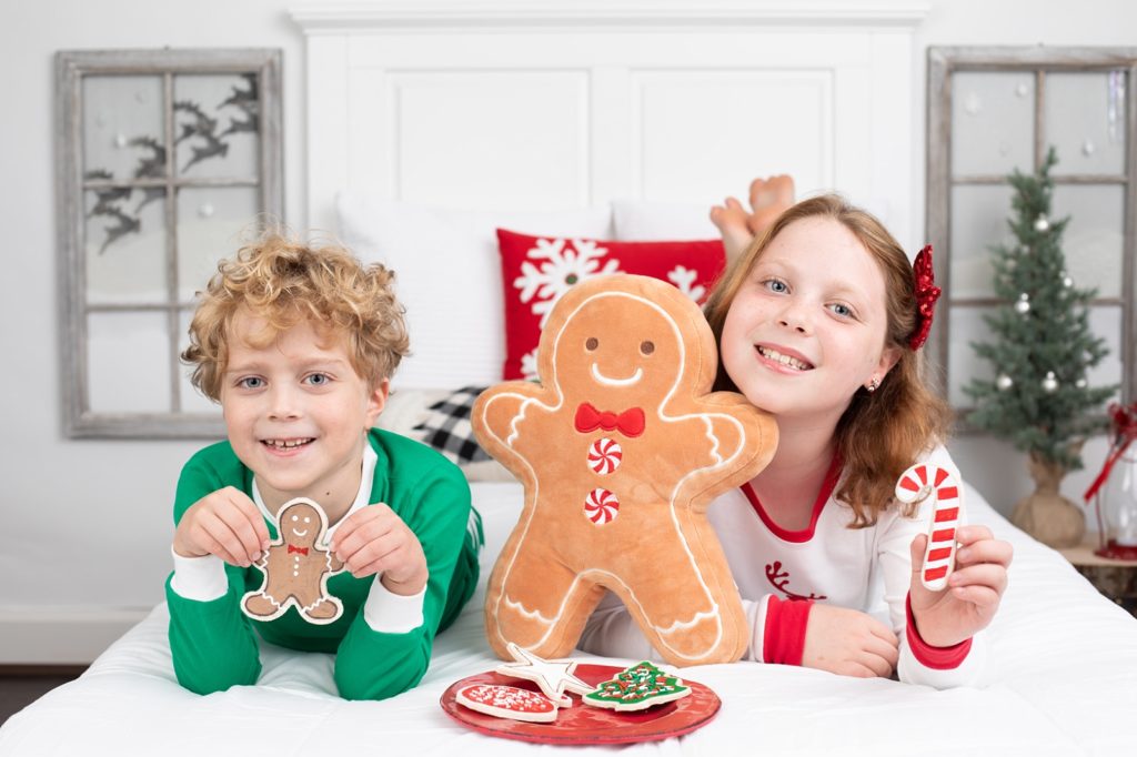 boy and girl holding pretend Christmas cookies on a bed with windows on the wall and Santa's reindeer flying outside
