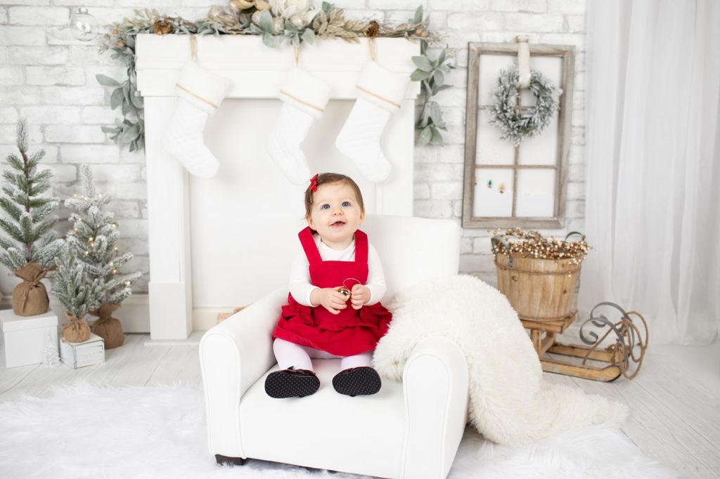 baby girl wearing a red dress and sitting in front of a fireplace
