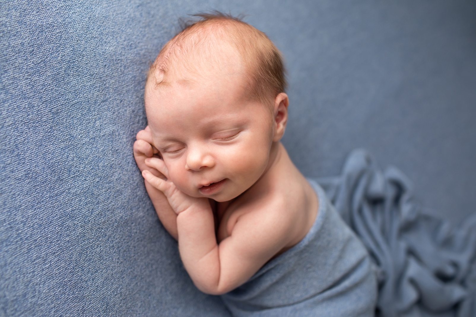 newborn boy with smile on blue fabric