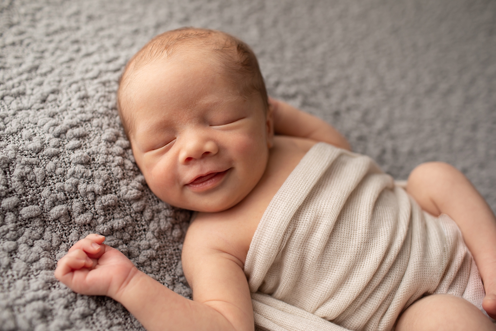 newborn boy on gray fabric smiling

