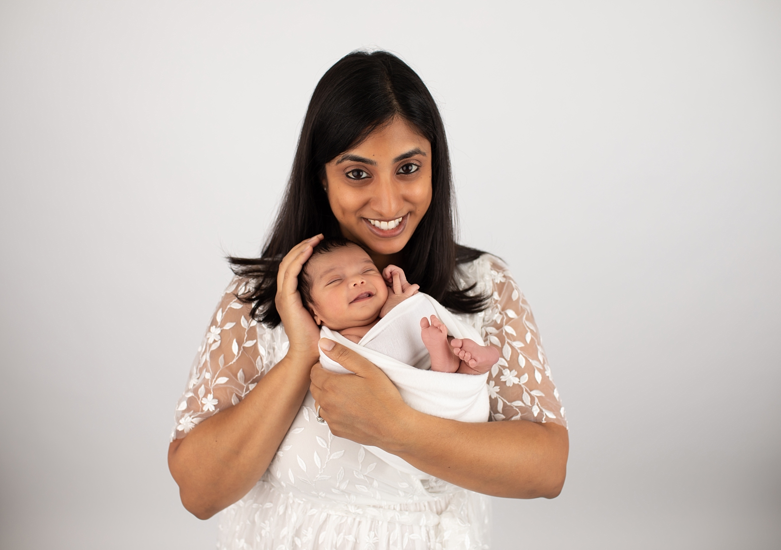 Smiling Newborn wrapped in white colored wrap and mom smiling at camera by Baltimore Newborn Photographer
