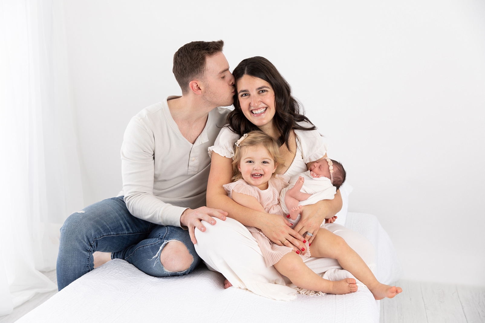 family of four smiling and holding newborn