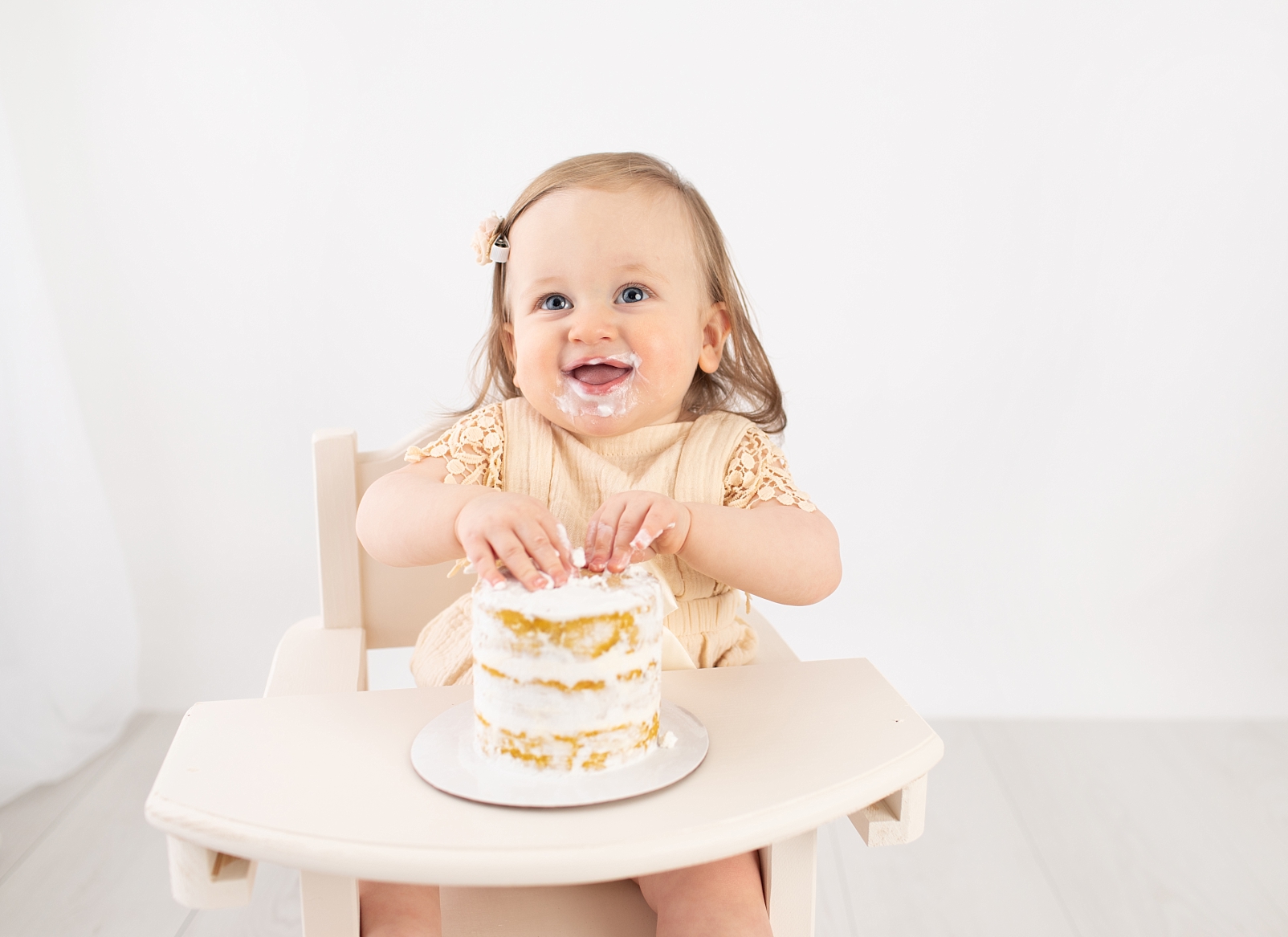 baby girl smiling in high chair with cake for first birthday portraits