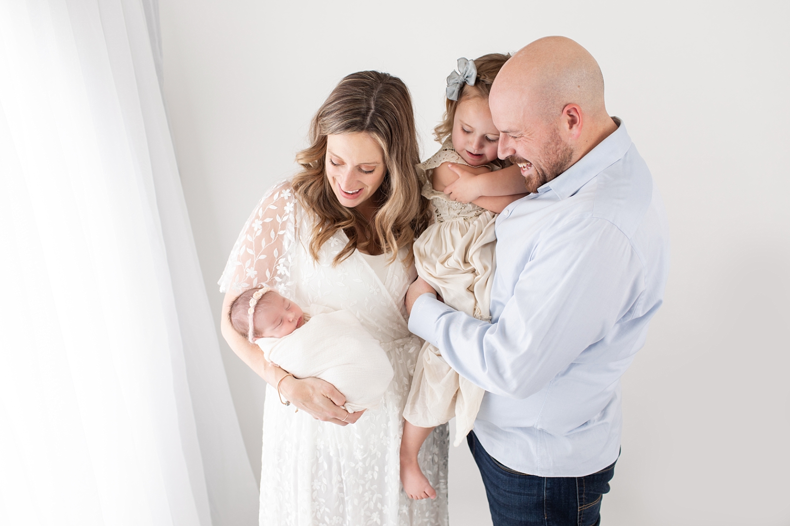 A mom, dad, sister and baby standing near bright white curtains | Ellicott City Newborn Photographer
