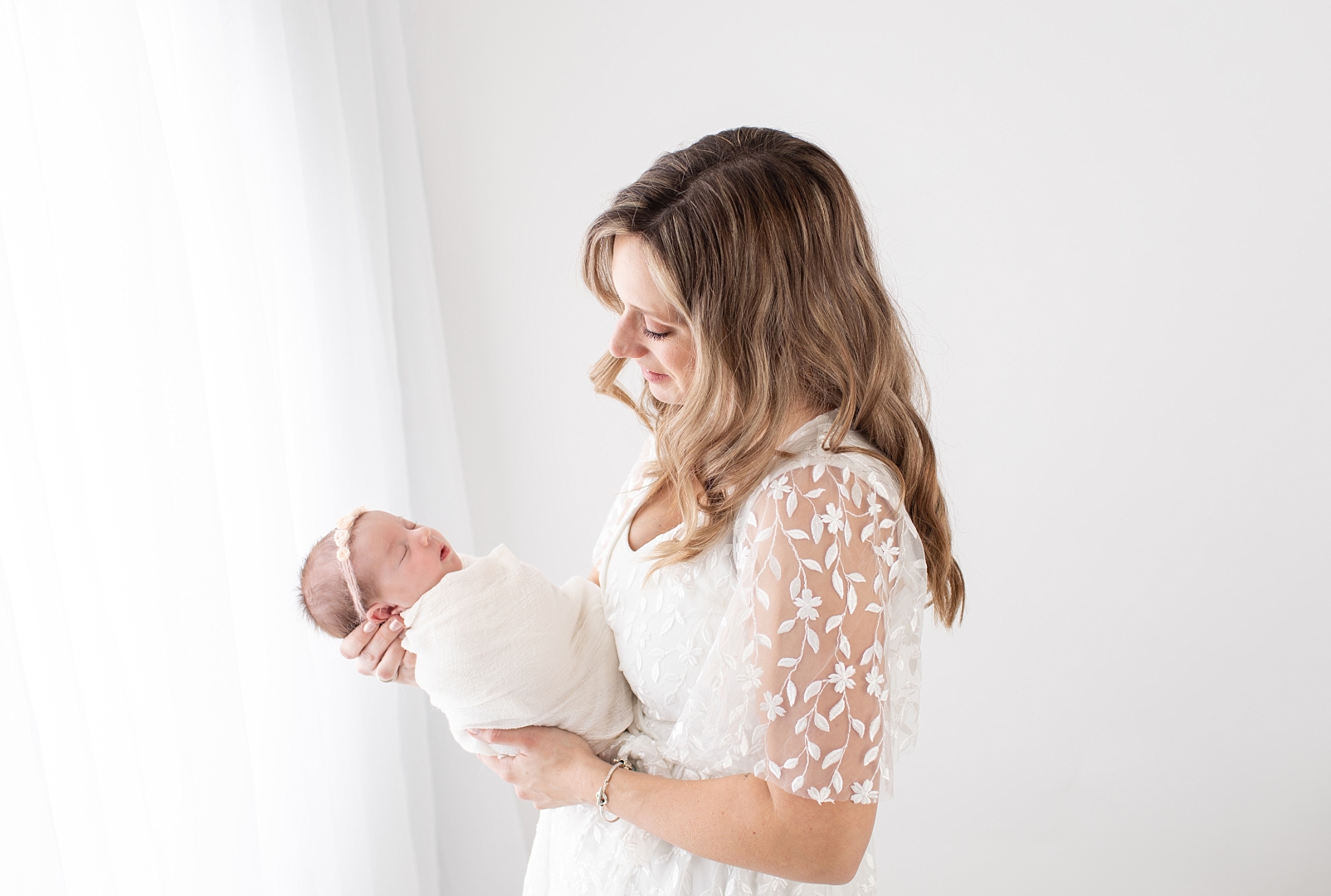 mom looking at baby girl newborn with white curtain light by Baltimore Newborn Photographer
