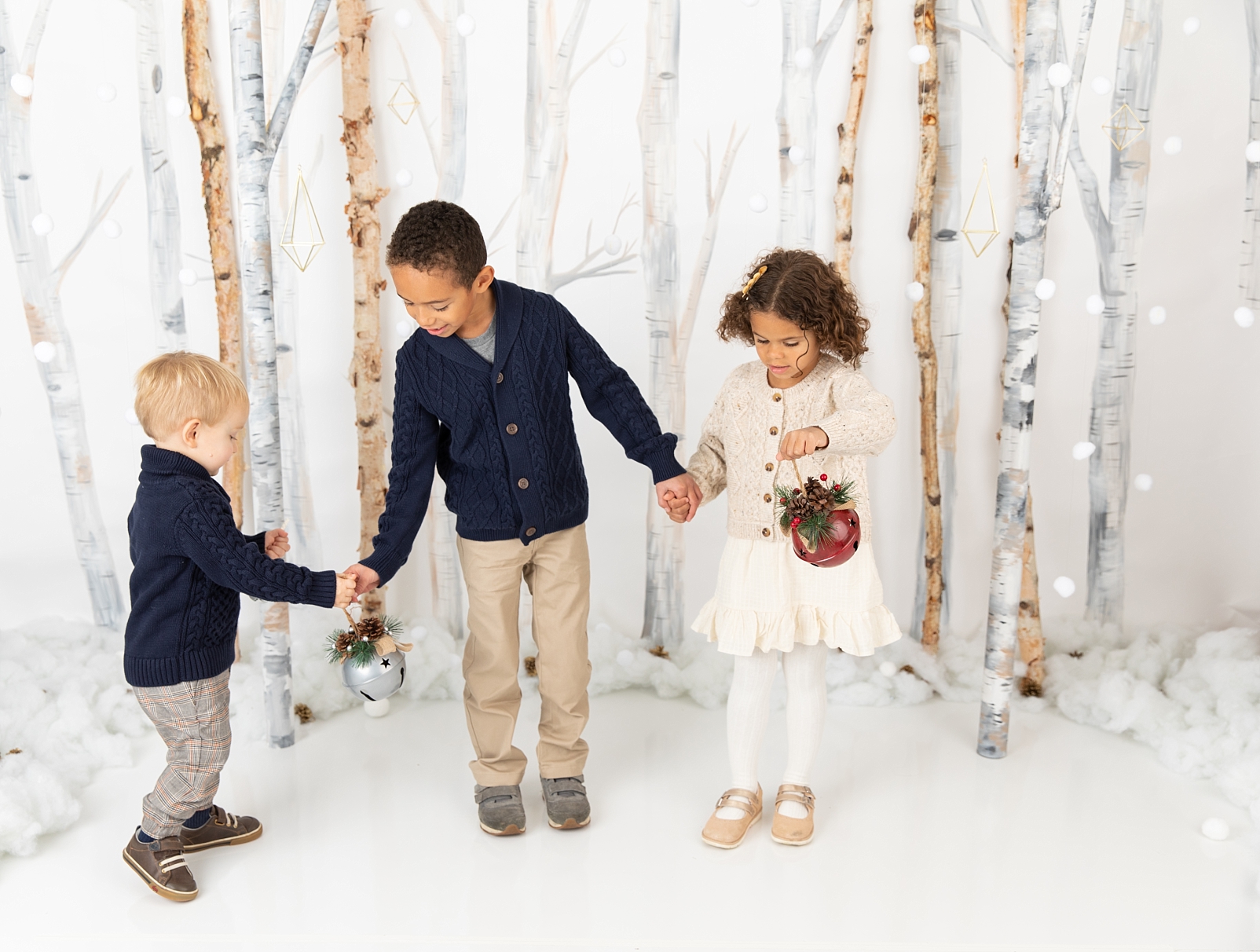 3 children standing in front of birch trees holding bells for Christmas minis in Ellicott City