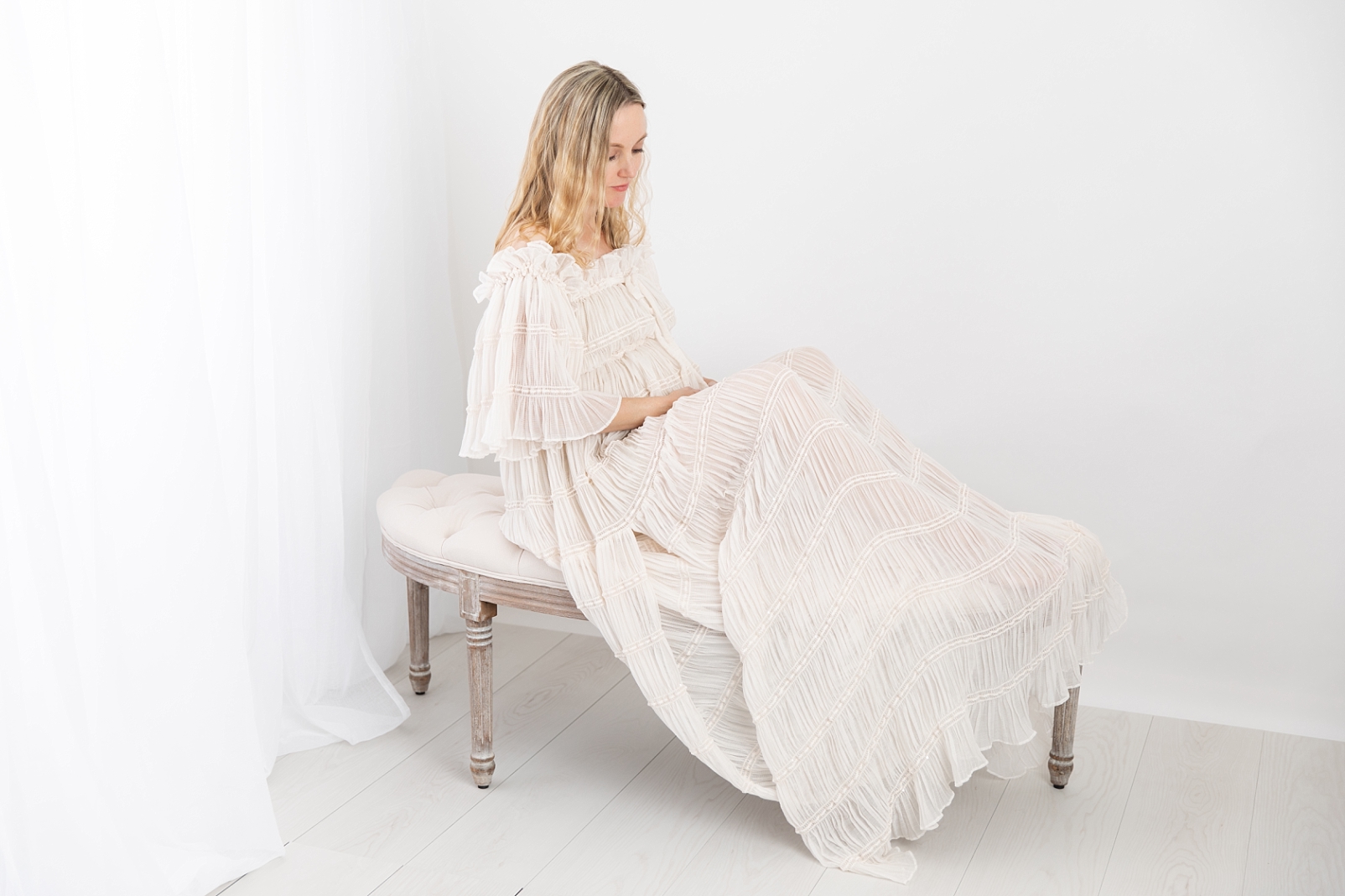 Pregnant mother in a beautiful gown sitting on a linen tufted bench in Ellicott City Maryland
