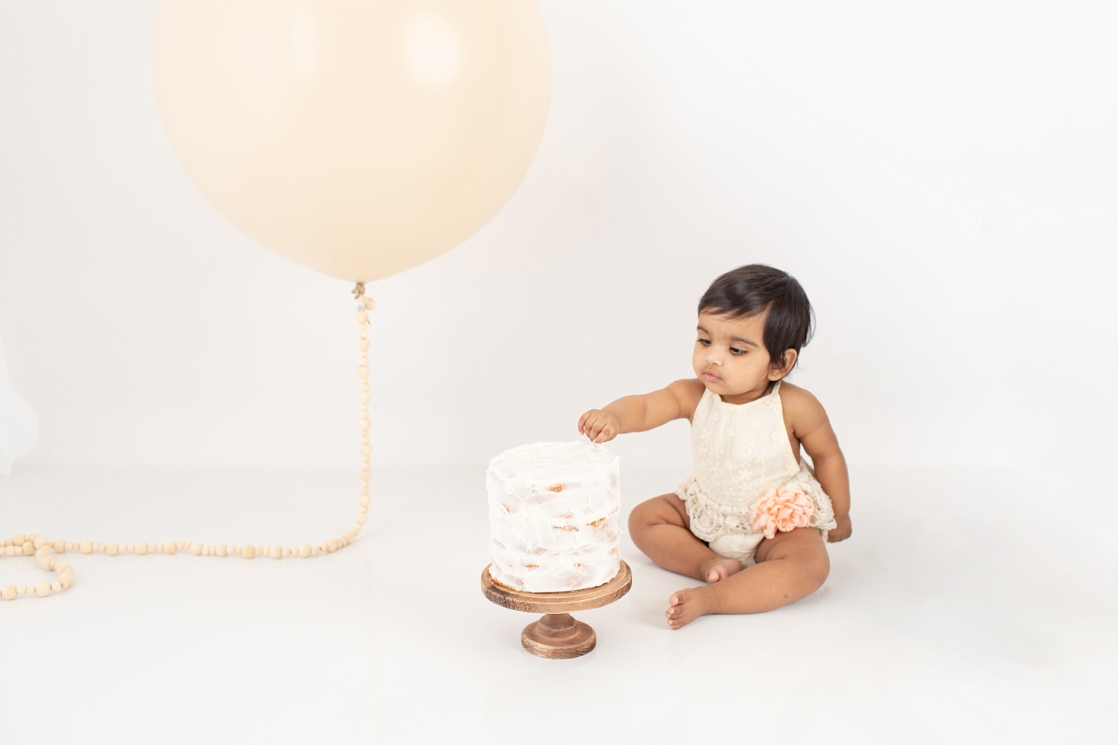 How to Choose a Smash Cake 6" cake with textured white icing and baby with decorative outfit and balloon eating cake

