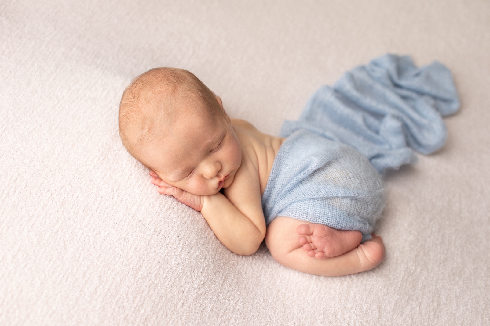 newborn boy wrapped in light blue fabric in tummy lying pose