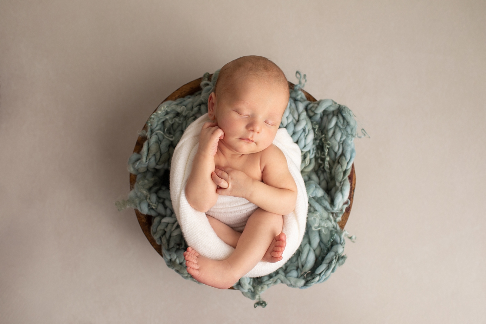 newborn boy wrapped in a white fabric in a brown wooden bowl