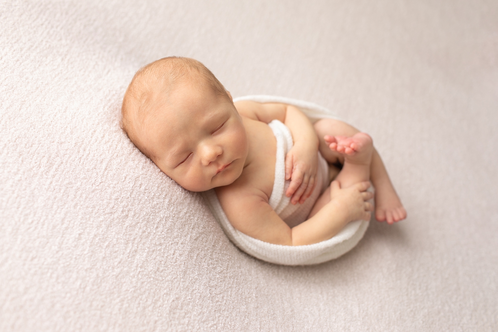 newborn baby boy in a white wrap lying on his back and why you should hire a professional newborn photographer