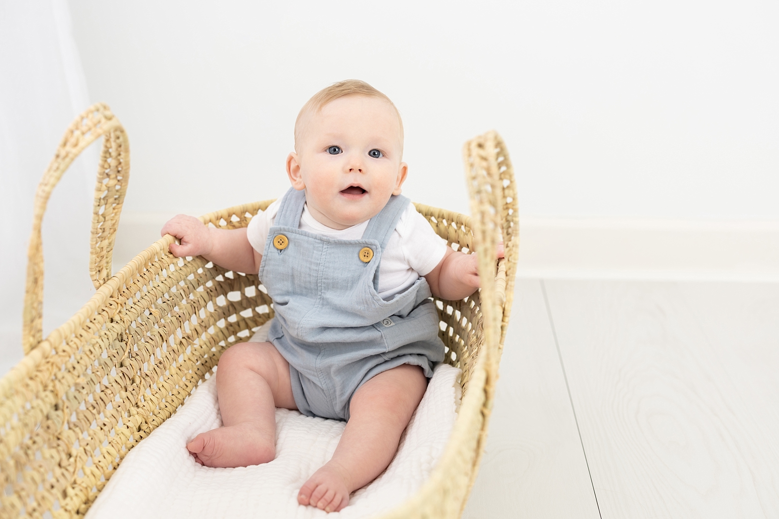 7 months milestone portraits of baby boy in light blue overalls in a basket
