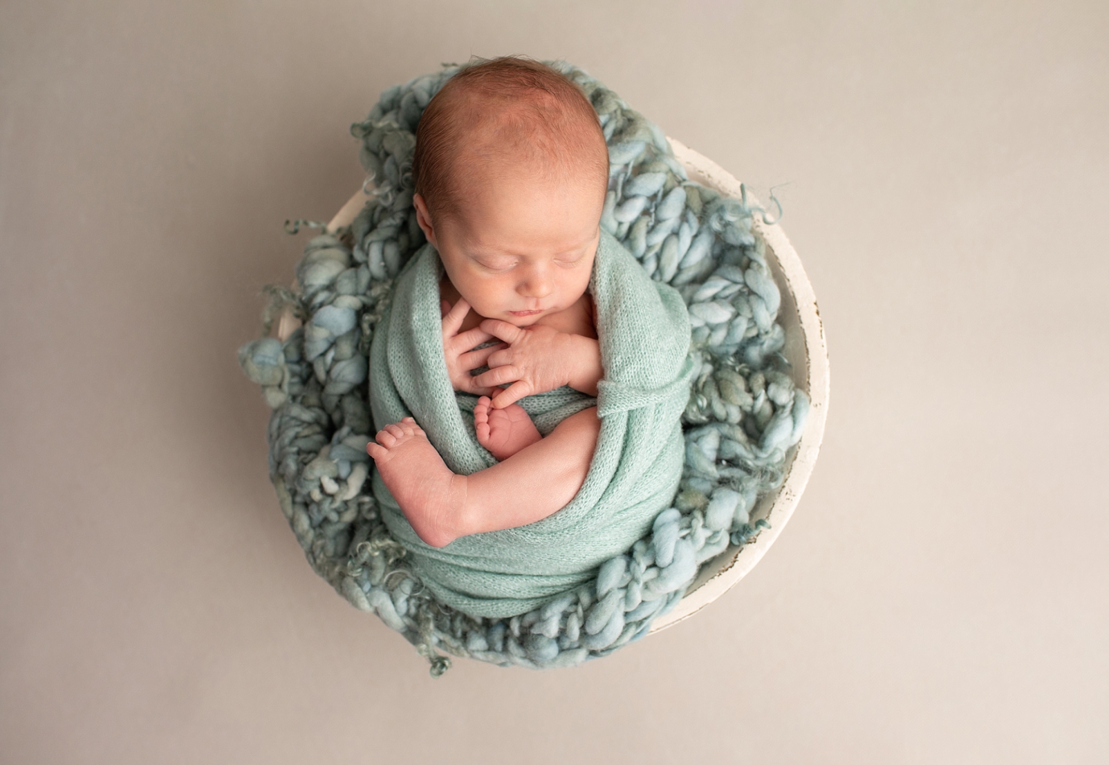 newborn boy sleeping and wrapped in a blue green wrap in a bowl