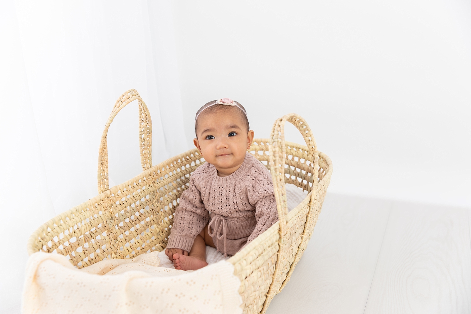 7 month old baby in a knit outfit sitting in a Moses basket taken during the First Year Membership with Maryland Baby Photographer