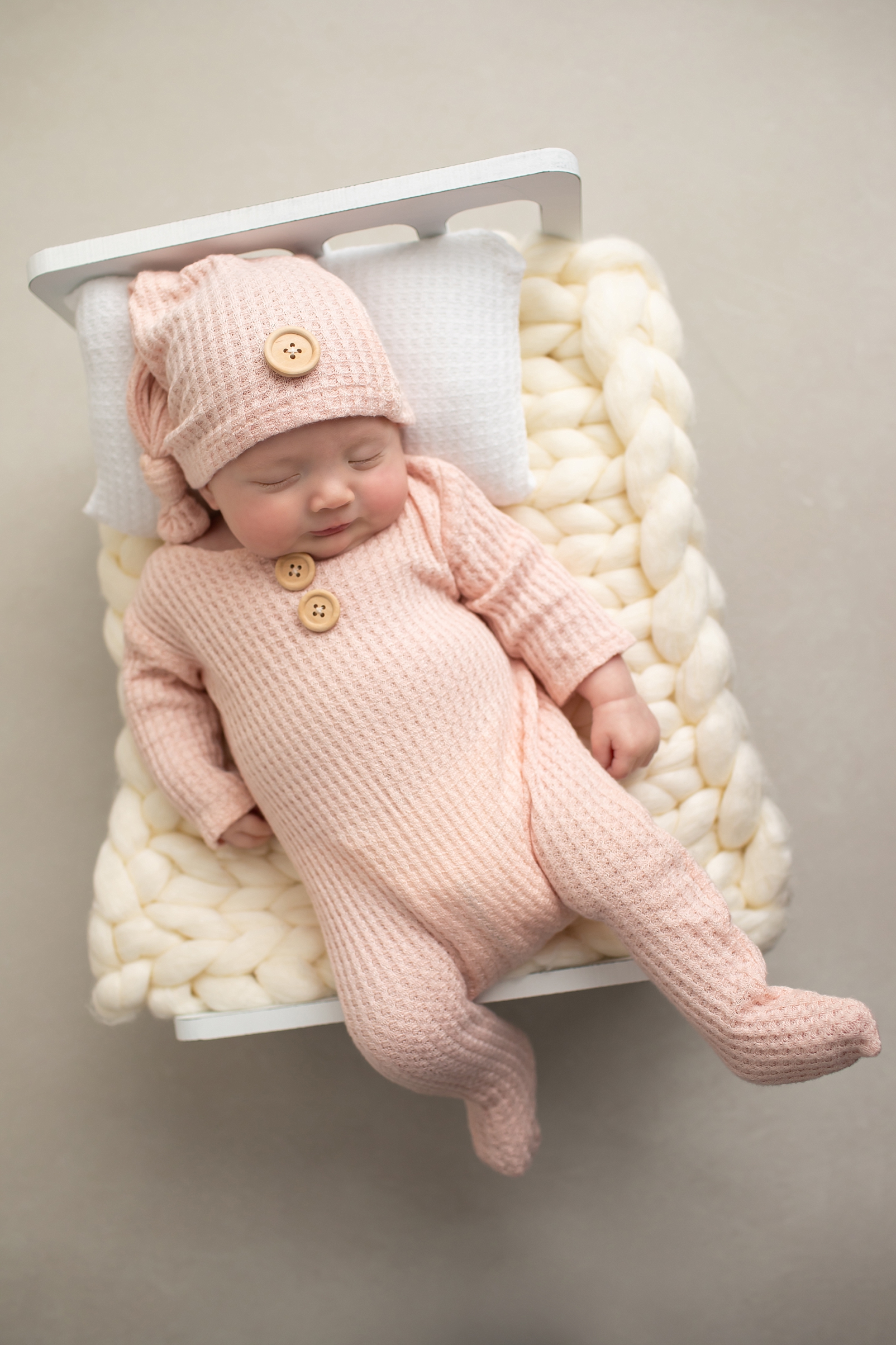 Newborn girl in pink pajamas with matching hat on a newborn bed