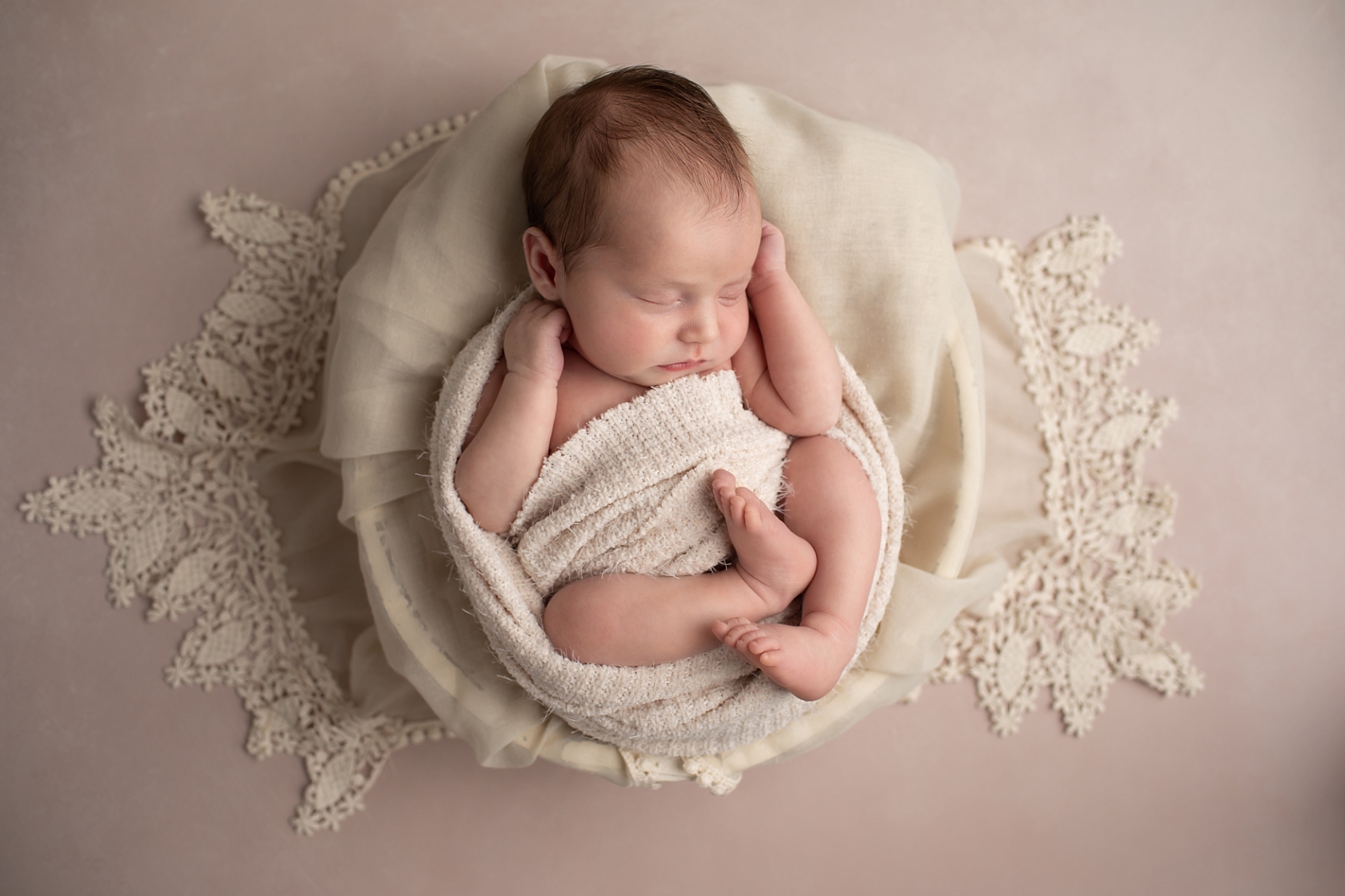 Newborn girl wrapped and posed in a bowl with lace