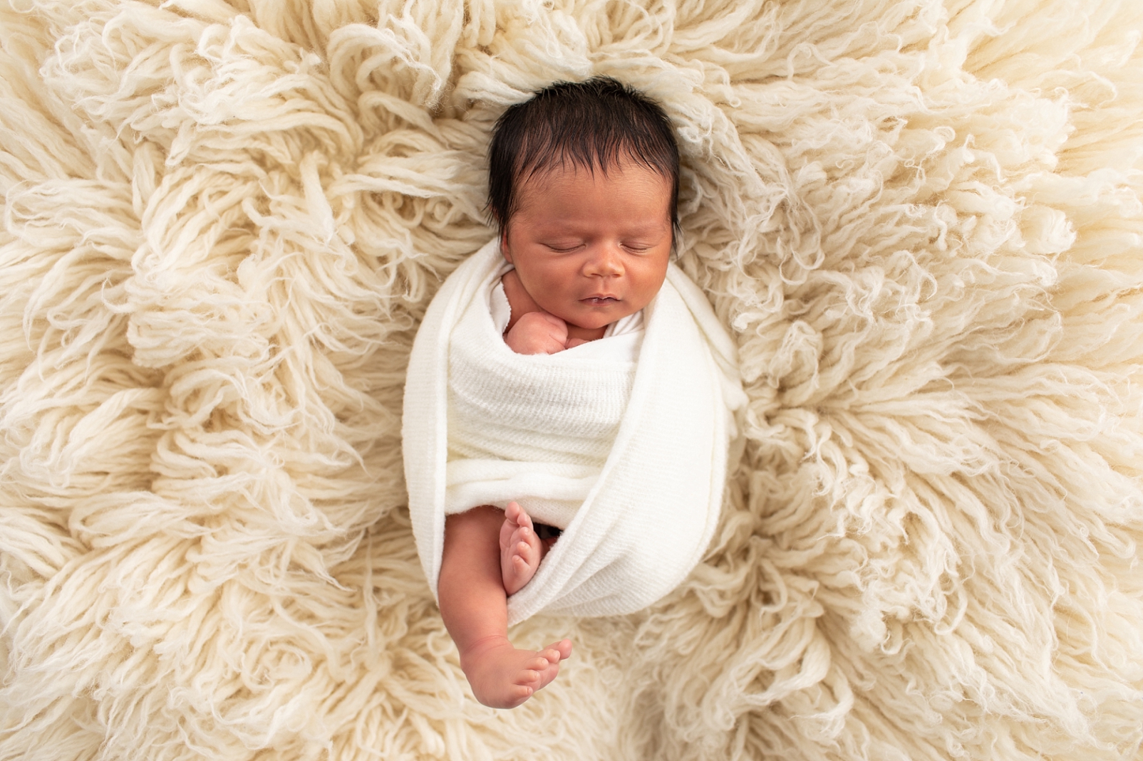 Newborn boy wrapped in white fabric on a flokati