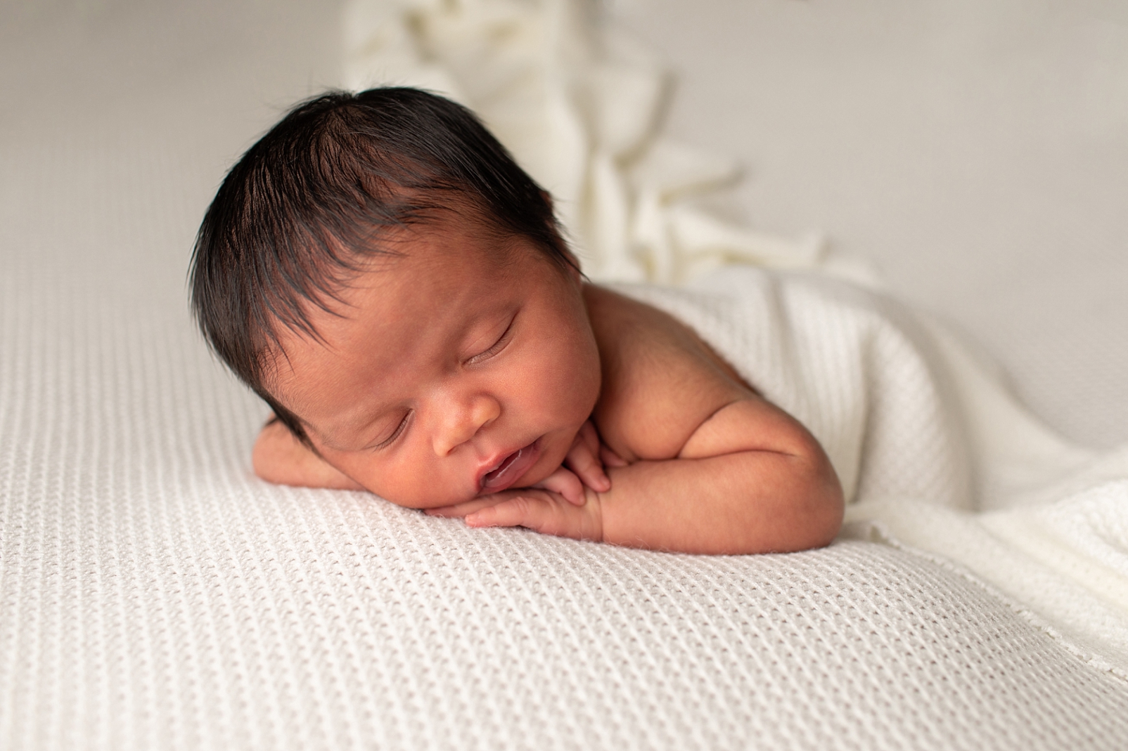 Newborn boy in tummy lying pose on a textured white fabric