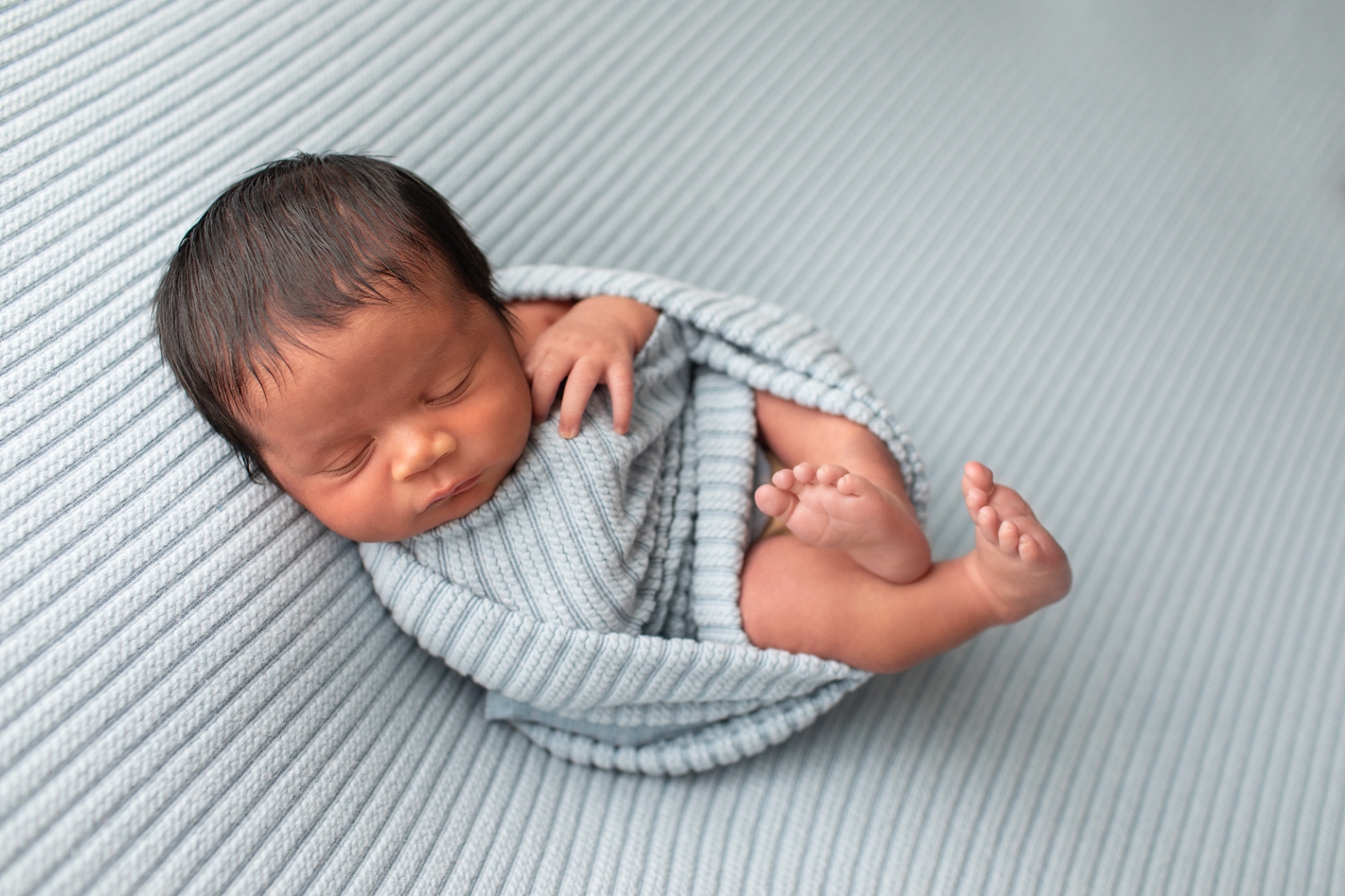 Newborn boy wrapped in ribbed light blue fabric on his back
